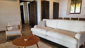 A living room with a white sofa, a wooden chair, a small wooden table, and a patterned rug. - Stunning Beachfront Home near Cambutal Beach Break (Ave María)