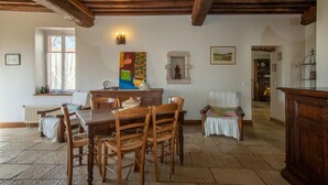 Un coin repas avec une table et des chaises en bois, une fenêtre avec des rideaux, un sol en pierre et un plafond rustique.
