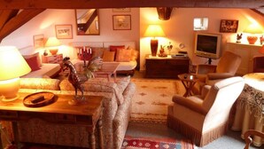A cozy attic room with wooden beams, a sofa set, a television, and various decorative items. - La Randonnée - FLEY - Gîte (FLEY)