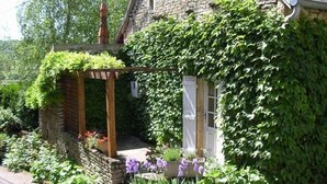 A stone house with a wooden porch and a garden with purple flowers. - La Randonnée - FLEY - Gîte (FLEY)