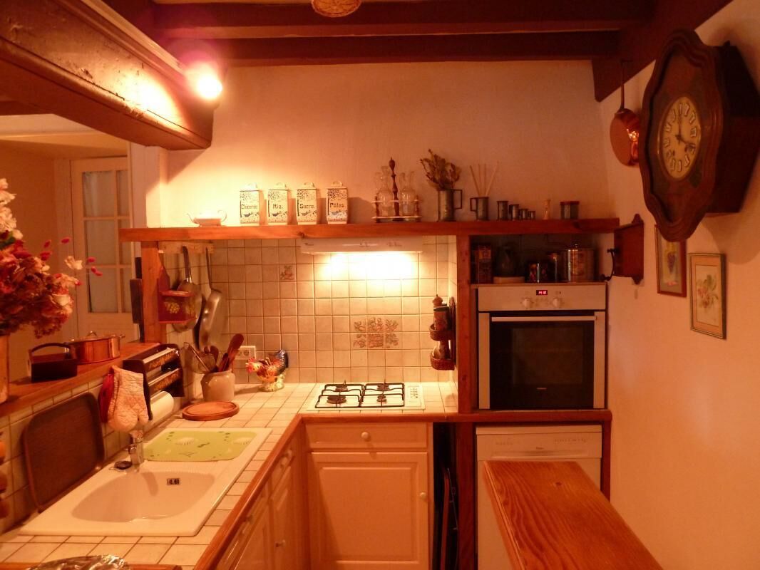 A kitchen with a gas stove, oven, and dishwasher. There is a sink, a wooden countertop, and a clock on the wall.