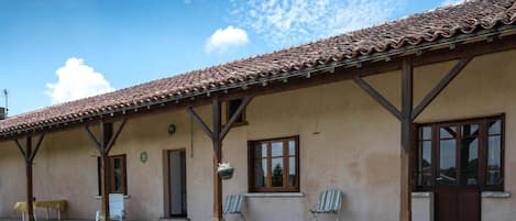 A building with a tiled roof, a covered porch, and a small outdoor seating area with chairs.