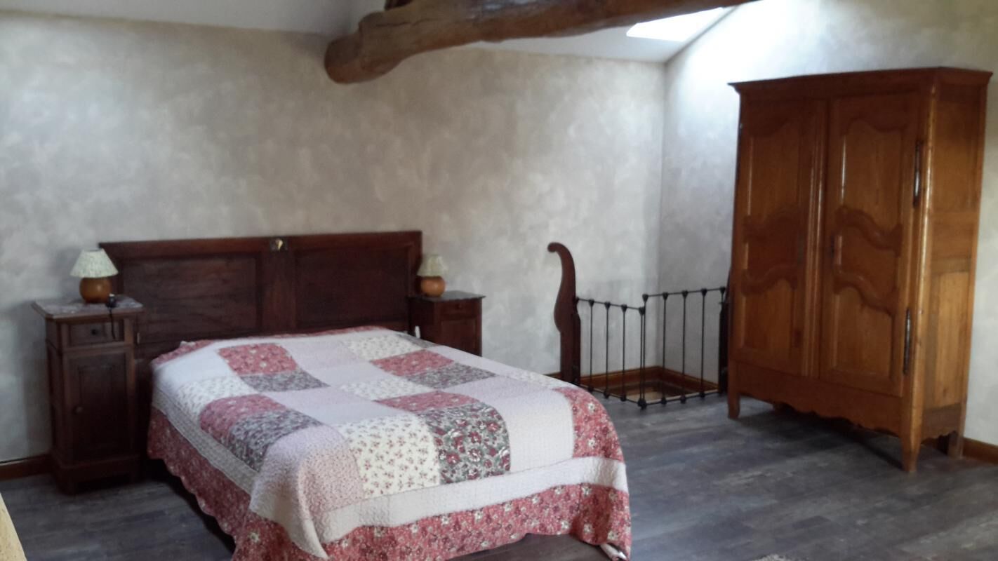 A bedroom with a wooden bed, a wooden wardrobe, and a small nightstand with a lamp.