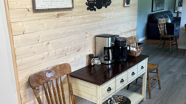 Una cocina acogedora con paredes de madera, una estación de café y un comedor con una silla y mesa de madera.