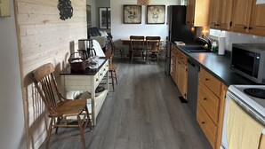 Una cocina con armarios de madera, una zona de comedor con sillas, una cafetera y un microondas.