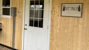 Entrada a una cabaña de madera con un letrero que dice 'Welcome' sobre la puerta y otro letrero en la pared.