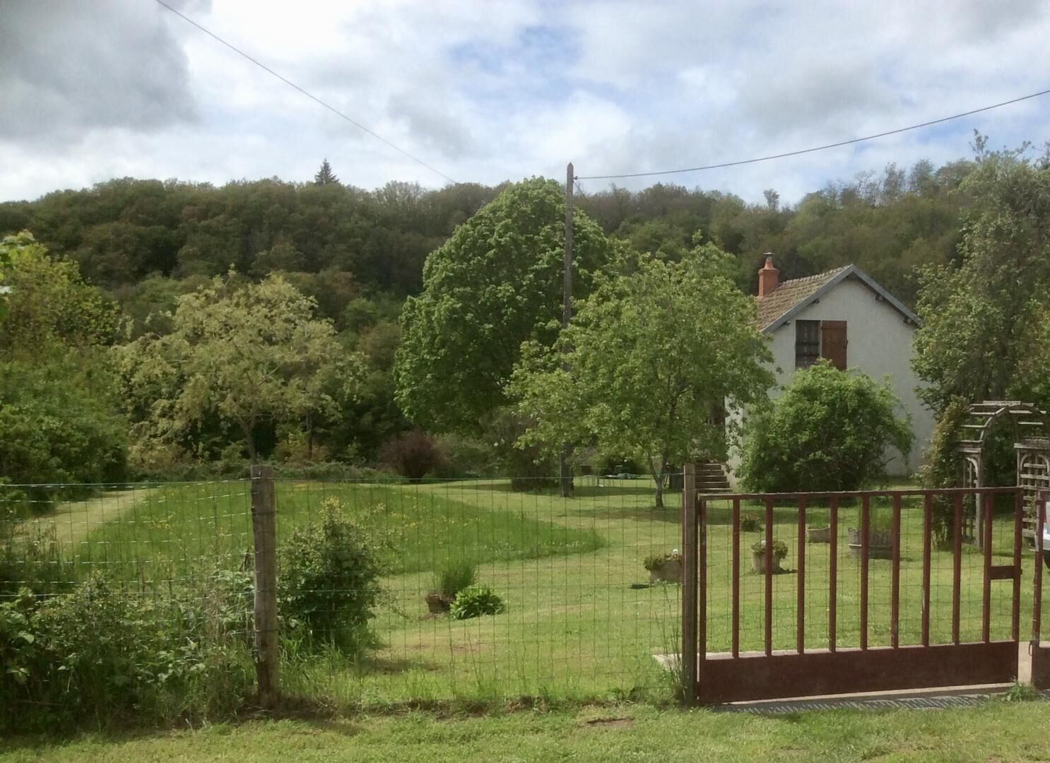 A rural house with a fenced yard, surrounded by trees and hills.