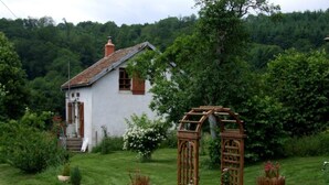 A white house with a red roof, surrounded by a lush garden with potted plants and a wooden arbor. - Le Tilleul - CHISSEY-EN-MORVAN (CHISSEY-EN-MORVAN)