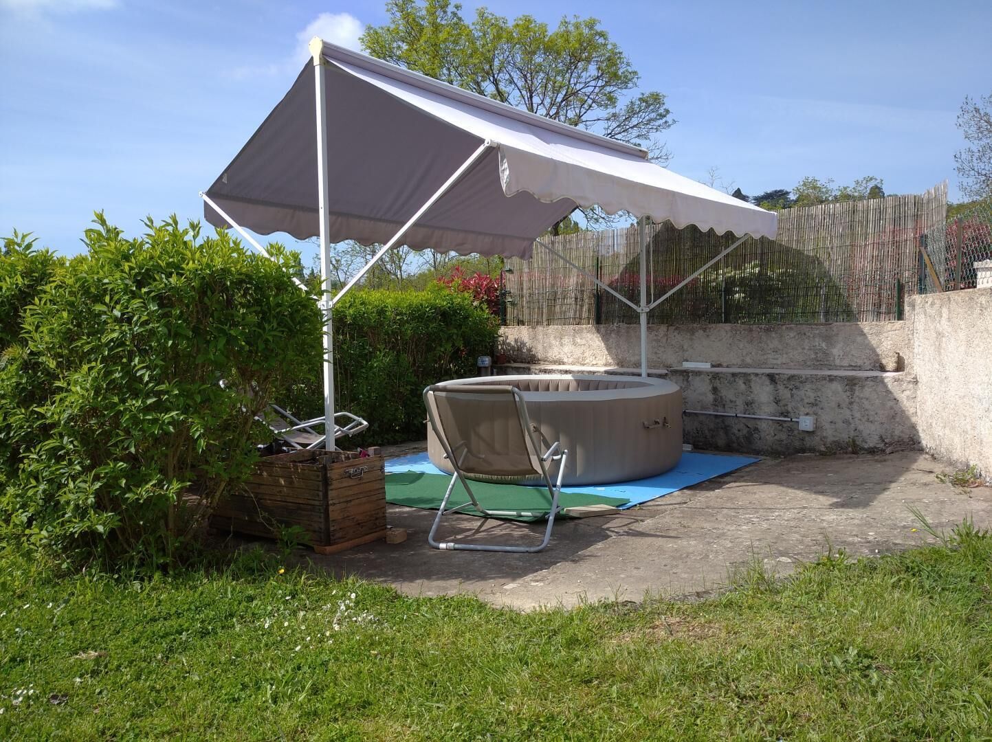 A covered outdoor area with a hot tub, a lounge chair, and a wooden structure.