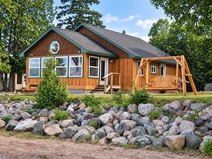 A wooden cabin with a porch, large windows, and a swing set.