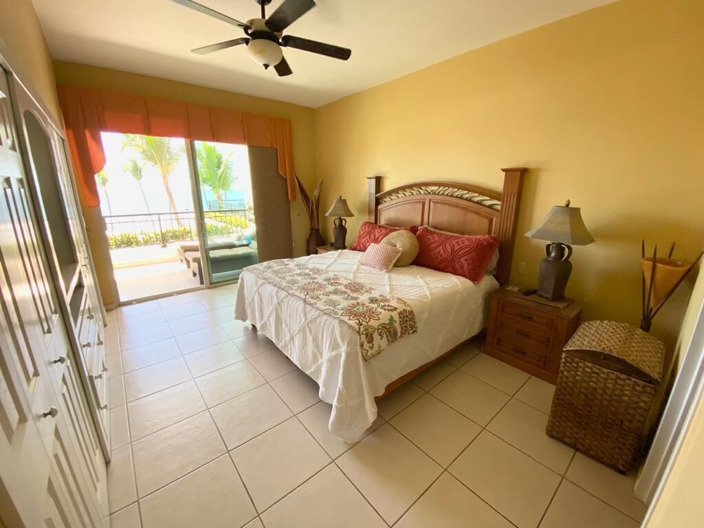 A bedroom with a bed, a ceiling fan, a nightstand, a lamp, and a wicker basket.