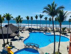 A pool area with a bridge, palm trees, and a beach view.