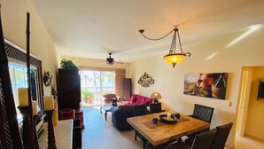 A spacious living area with a wooden dining table, wicker furniture, and a ceiling fan.