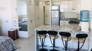 A compact kitchen with a marble countertop, four bar stools, a refrigerator, and a water dispenser. - Aria Ocean Beachfront Condos (Nuevo Nayarit)