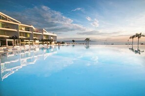 A modern hotel with a large infinity pool, multiple balconies, and a view of the ocean. - Aria Ocean Beachfront Condos (Nuevo Nayarit)