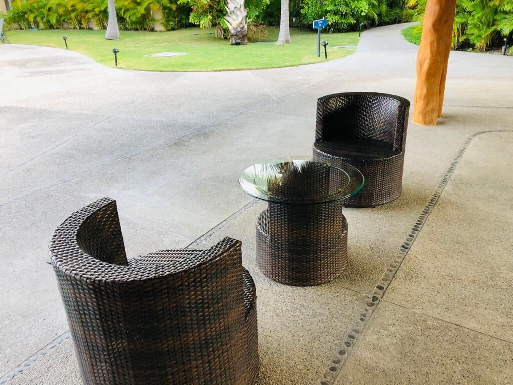 Drie rieten stoelen met glazen tafelblad op een betonnen terras.