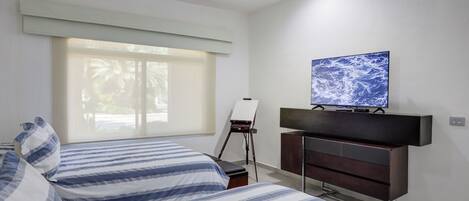 A bedroom with a bed, a dresser, a painting on a easel, and a television on the wall.