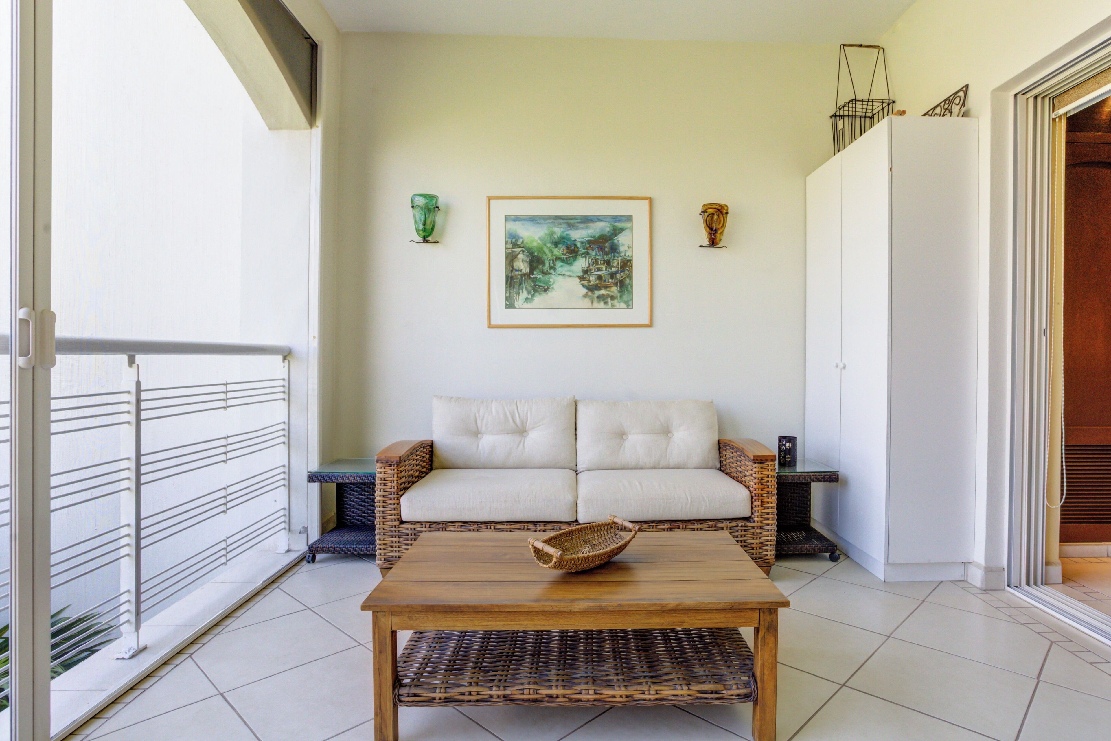 A balcony with a white sofa, a wicker table, and a framed painting on the wall.