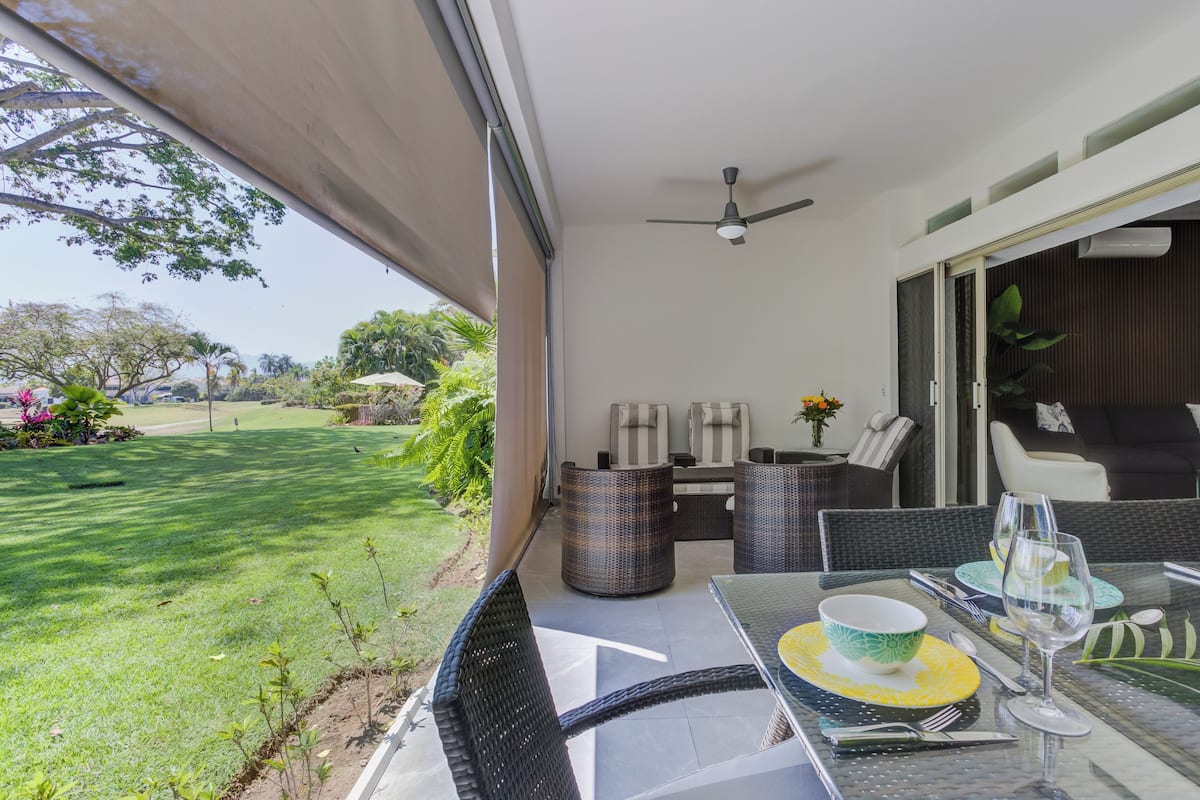 A patio with a table set for dining, outdoor furniture, and a view of a grassy area with trees.