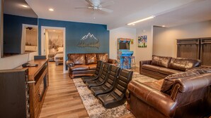 A living room with leather sofas, a coffee table, a TV, and a mountain mural on the wall.