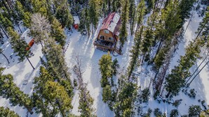 An aerial view of a cabin surrounded by snow-covered ground and trees.