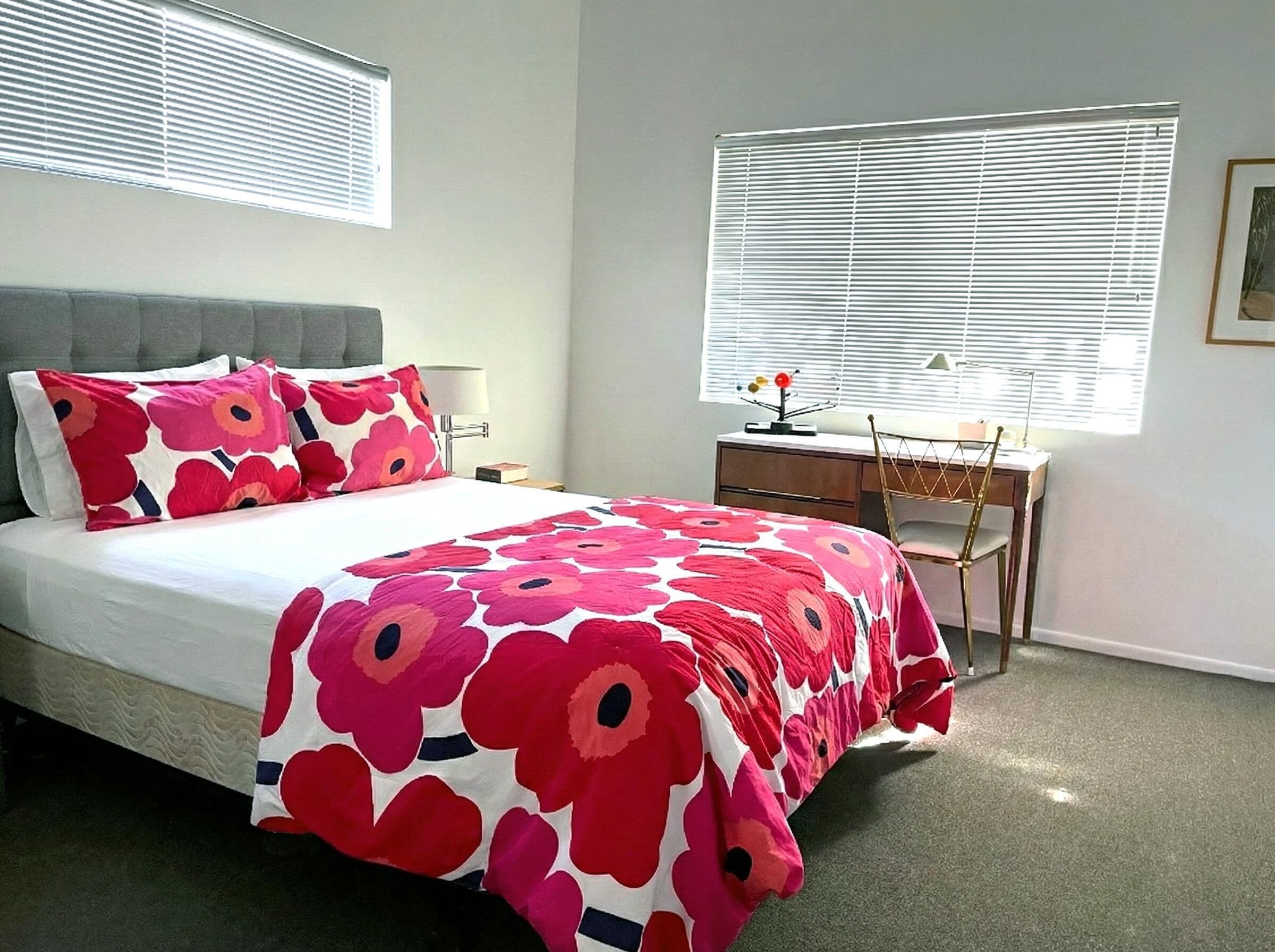 A bedroom with a bed, a desk, and two windows with blinds.