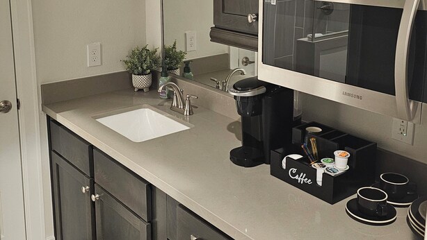 A modern kitchen with dark cabinetry, a stainless steel refrigerator, a built-in microwave, and a coffee station.