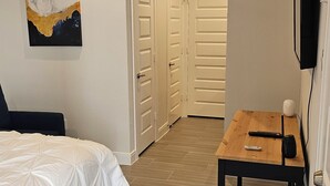 A bedroom with a bed, a desk, and a chair. There are two doors leading to another room.