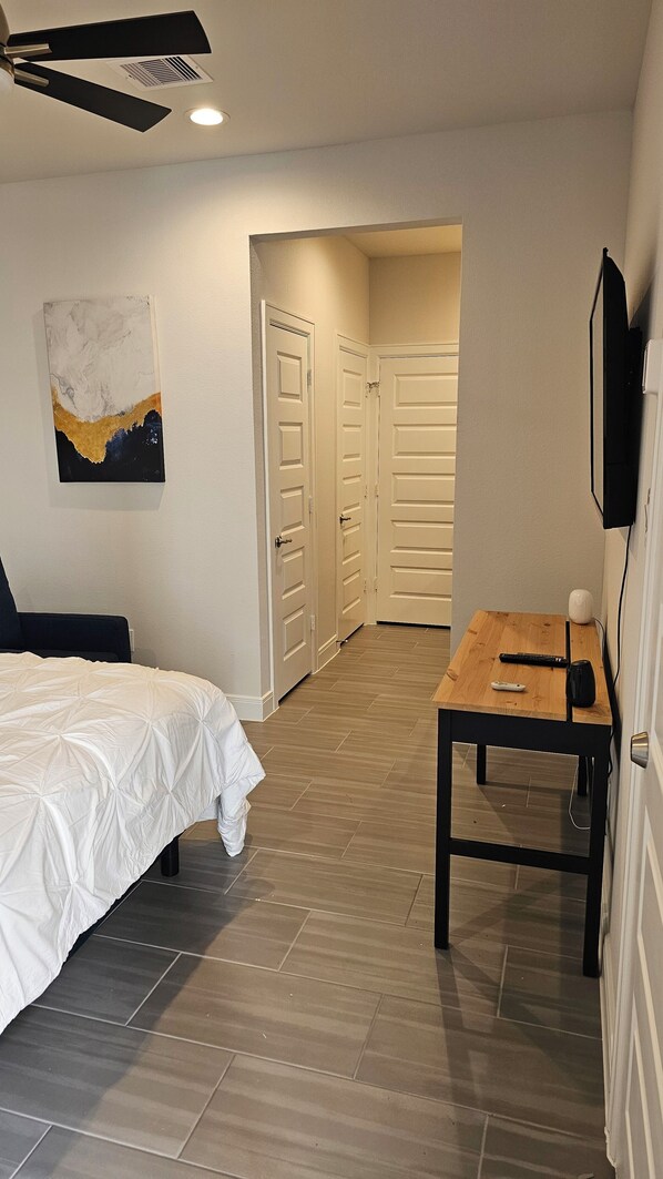 Un dormitorio con cama, escritorio y silla. Hay dos puertas que dan a otra habitación.