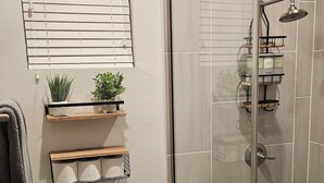 A modern bathroom with a glass shower enclosure, a toilet, and a window with blinds.