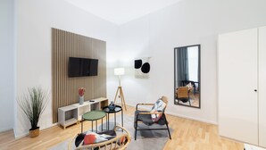 Een moderne woonkamer met een flatscreen televisie, een staande lamp, een grote spiegel en een rieten stoel.