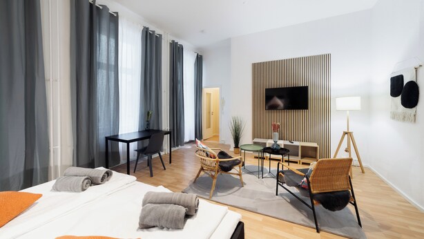 Een moderne hotelkamer met een bed, twee stoelen, een bureau, een televisie en een lamp.