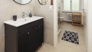 Een moderne badkamer met een zwart wastafelmeubel, twee spiegels, een witte wasbak en een douchecabine met glazen wanden.