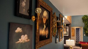 Una habitación con una pared azul, un retrato enmarcado, una lámpara y una mesa de billar.
