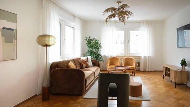 Ein modernes Wohnzimmer mit einer Couch, Sesseln, einem Couchtisch und einer Stehlampe.