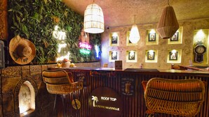 Un espace bar avec des chaises en osier, un panneau néon, des tableaux encadrés et une horloge au mur.