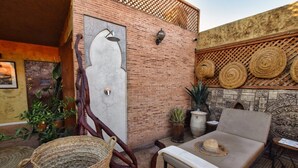 Un espace de détente extérieur accueillant, avec un fauteuil rembourré, un panier en osier et un mur décoratif orné de motifs circulaires.