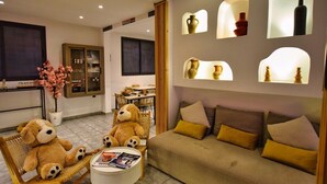 Un salon chaleureux avec un canapé, deux fauteuils et une table sur laquelle sont posés des magazines. On y trouve également des étagères décoratives ornées de vases et d’une plante en pot.