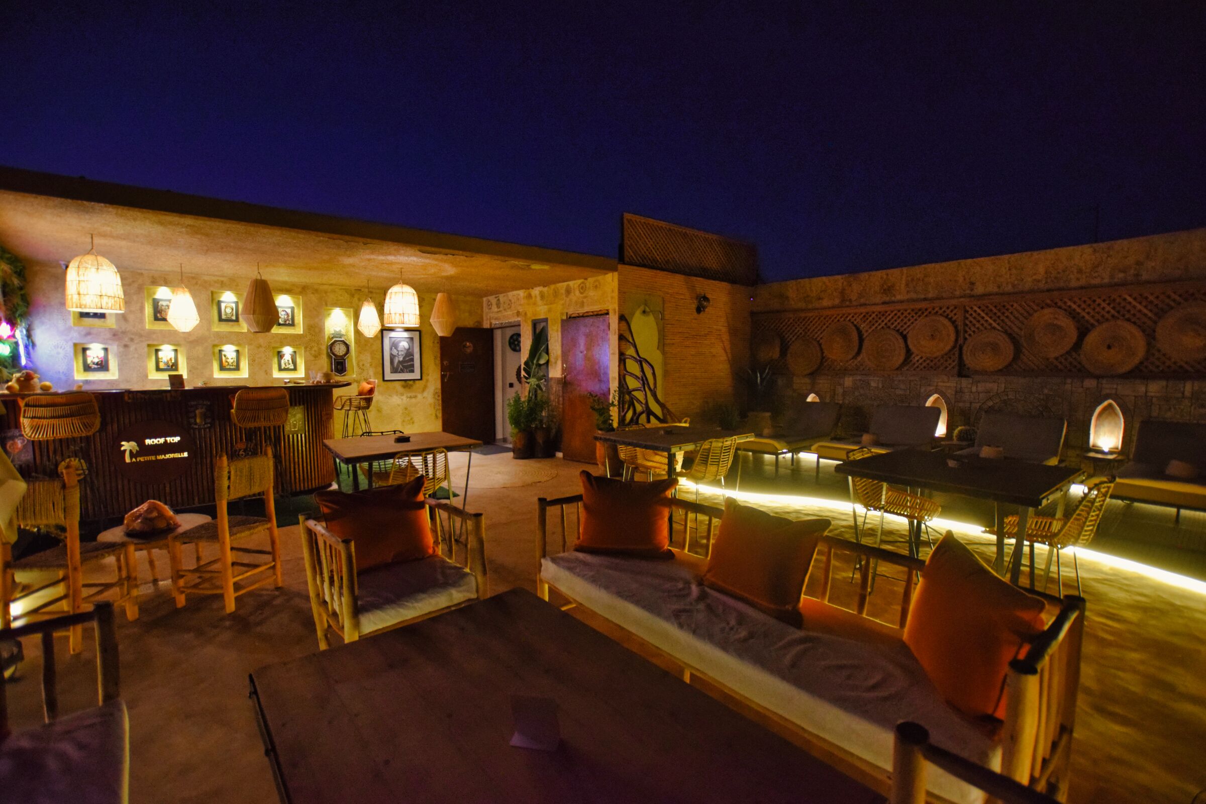 Un espacio al aire libre con mesas, sillas, una barra y luces fijadas a la pared.