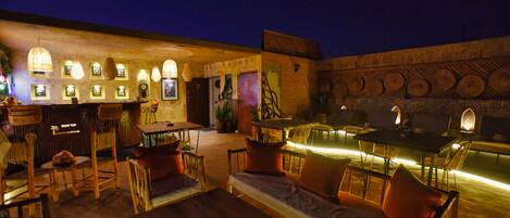 Un espacio al aire libre con mesas, sillas, una barra y luces fijadas a la pared.