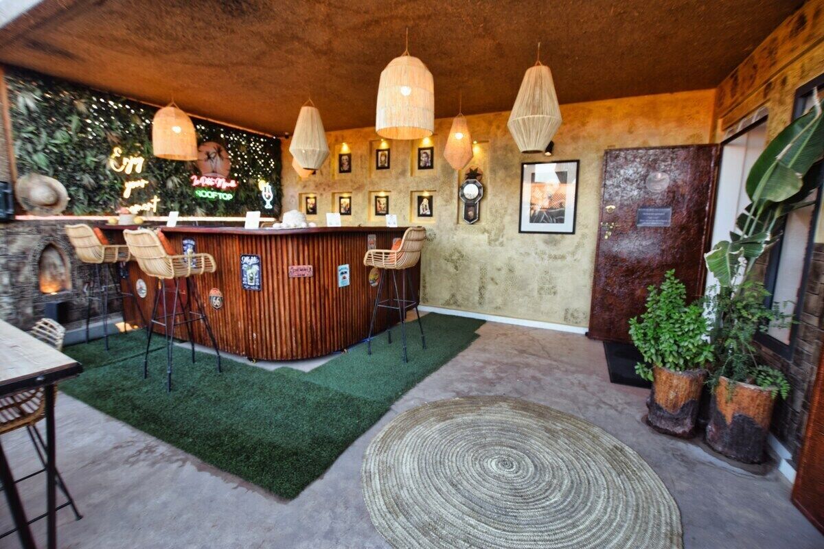A bar area with a wooden counter, wicker chairs, hanging pendant lights, and a green artificial turf rug.
