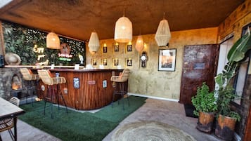 Una zona de bar con mostrador de madera, sillas de mimbre, lámparas colgantes y un felpudo de césped artificial verde.