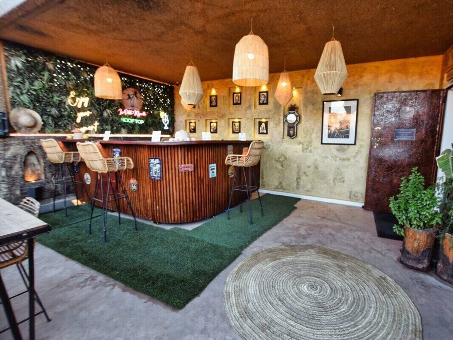 Una zona de bar con mostrador de madera, sillas de mimbre, lámparas colgantes y un felpudo de césped artificial verde.