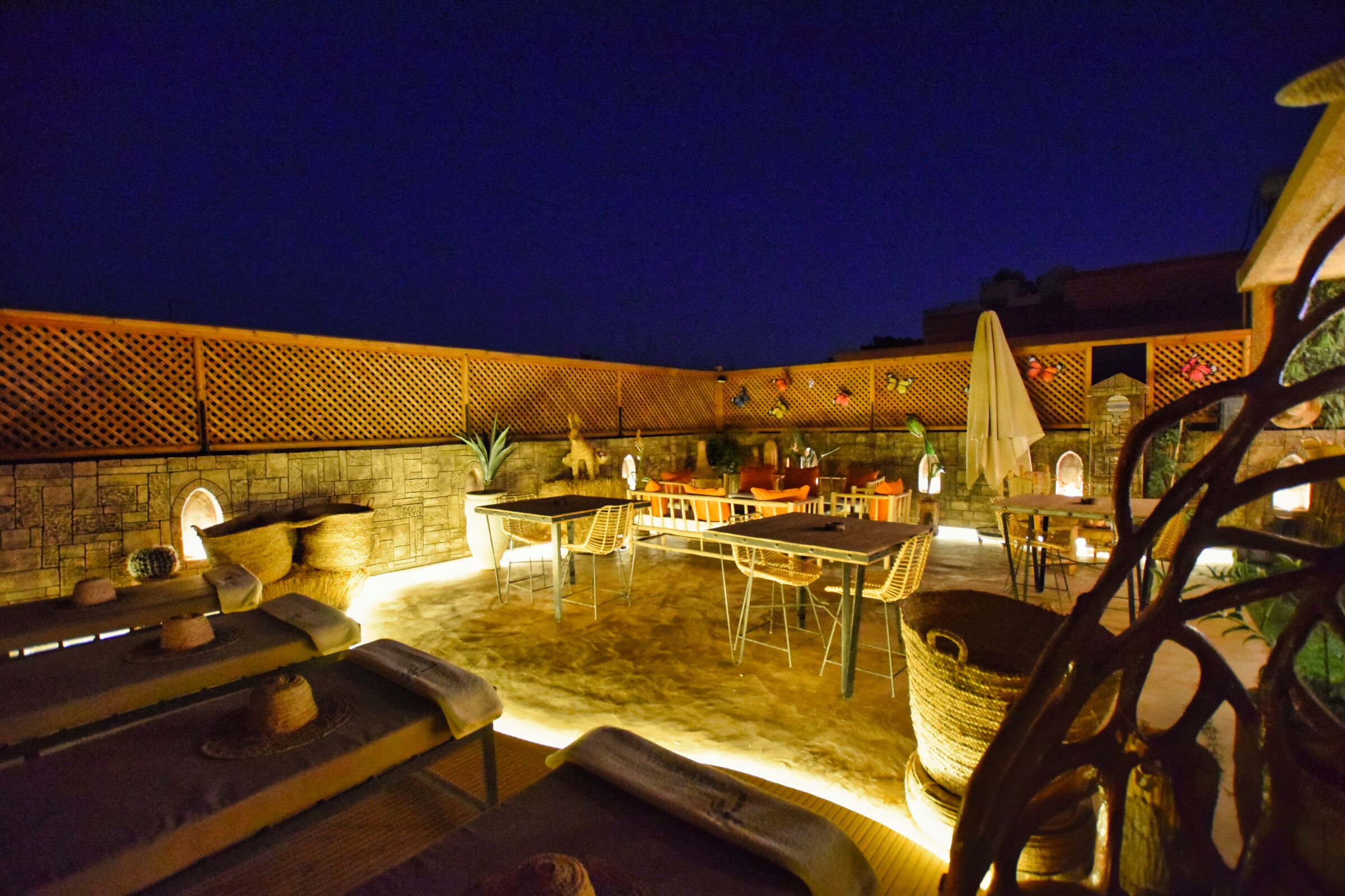Un espace extérieur aménagé en terrasse, avec des murs en pierre, des tables, des chaises et un coin salon doté de coussins.