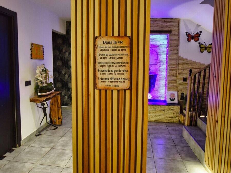 A hallway with vertical wooden slats, a sign with French text, a staircase with a butterfly decoration, and a wall with a stone pattern.