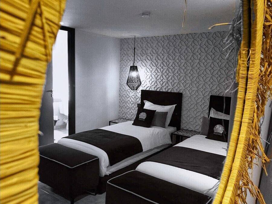 Un dormitorio moderno con dos camas, un muro con estampado geométrico y una lámpara colgante.