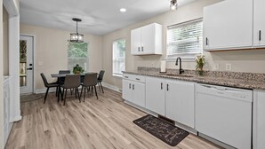 Une cuisine moderne avec des meubles blancs, un plan de travail en granit et un coin repas comprenant une table et des chaises.