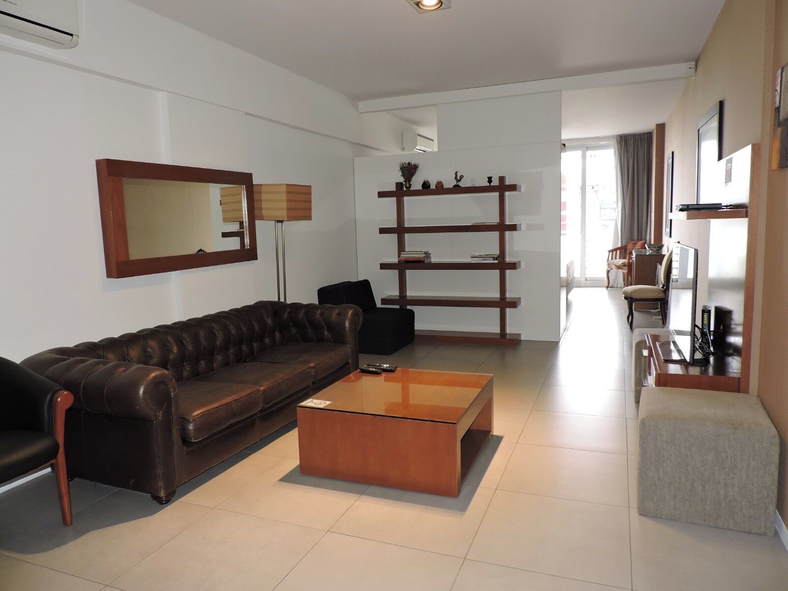 Een moderne woonkamer met een leren bank, een houten salontafel, een boekenkast en een eethoek met een tafel en stoelen.
