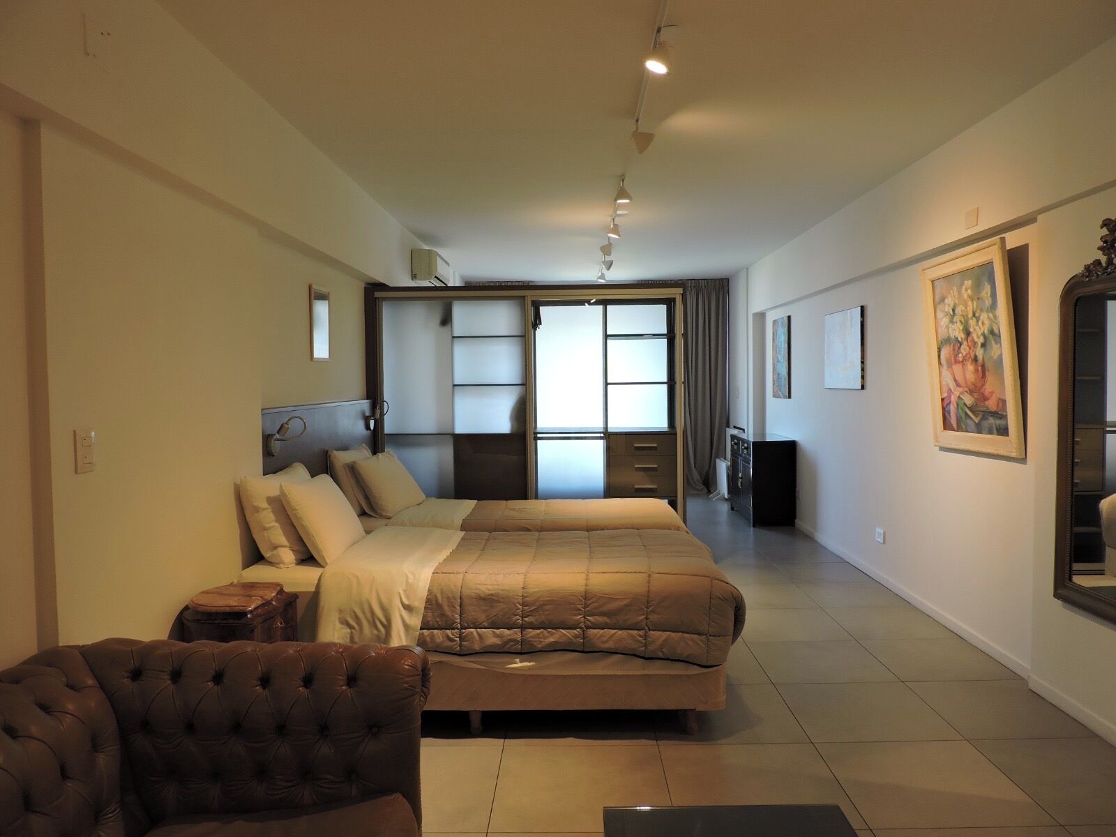 A spacious hotel room with a large bed, a leather armchair, a desk, and a sliding door leading to a balcony.