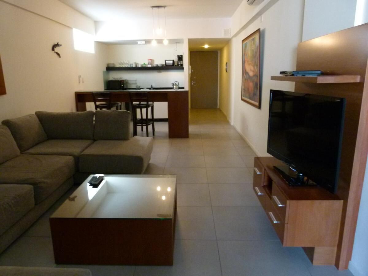 Een woonkamer met een bank, salontafel, televisie en een keuken op de achtergrond.